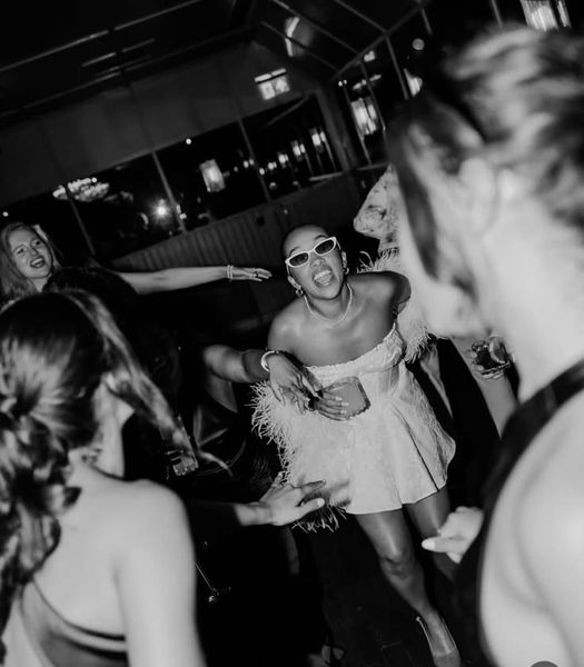 A bride to be in white sunglasses dancing with friends, in black and white