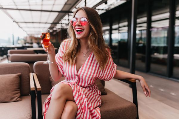 A woman in a striped dress and heart sunglasses laughing with a glass of rose