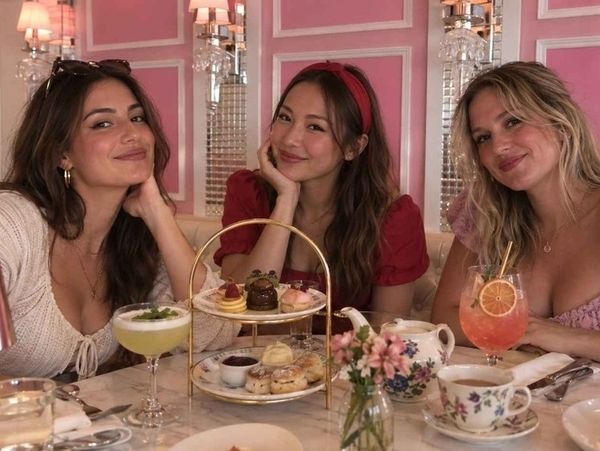 Three friends at a pink high tea with a tiered stand of sweets, a teapot and cocktails