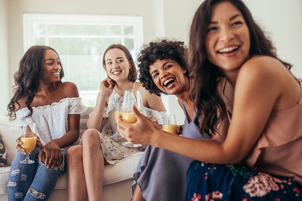 Four lovely ladies are smiling, holding a champagne glass, and having a great time while lounging on a couch