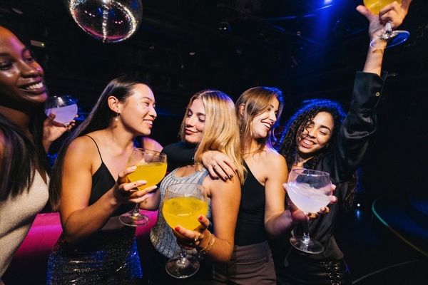 Friends laughing and raising cocktails under a disco ball
