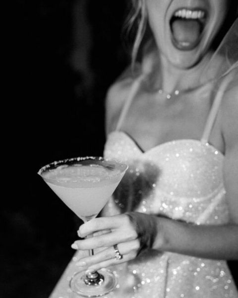 A bride to be in a sparkly dress laughing with a margarita, in black and white