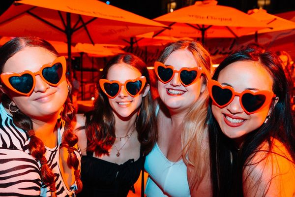 Four friends in orange heart sunglasses posing under red umbrellas at night
