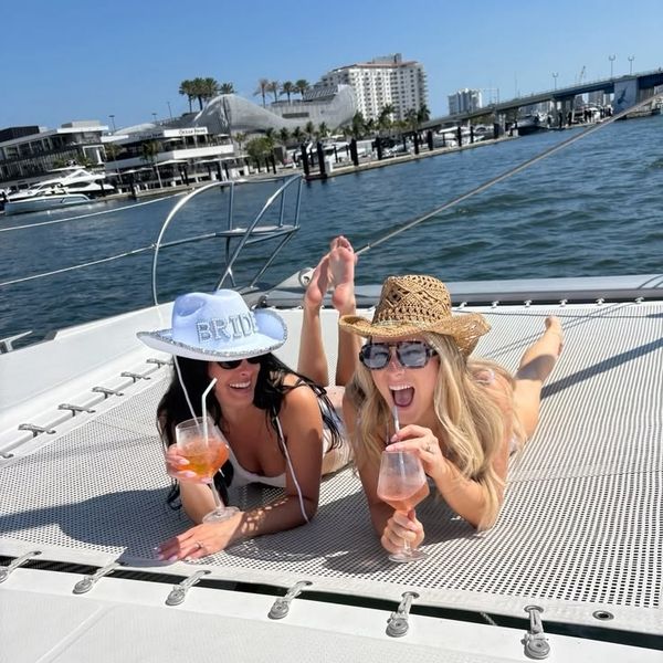 Two friends lying on a catamaran net with cocktails and party hats