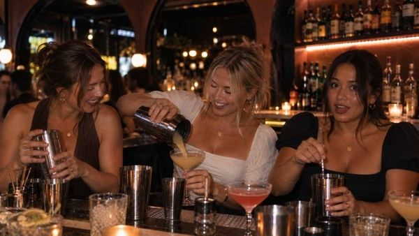 Three friends making cocktails side by side at a candlelit bar