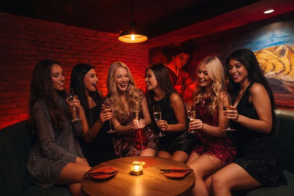 Seven women with glasses of bubbly around a candlelit table in a moody room