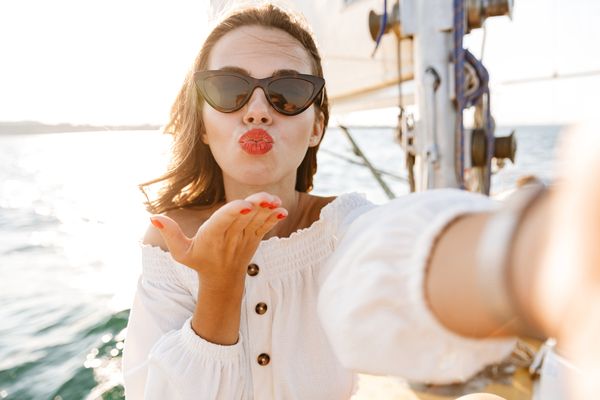 A woman in heart sunglasses blowing a kiss on a sailing boat