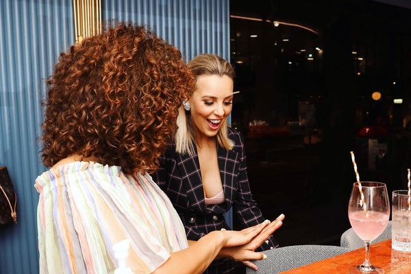Two women laughing at a marble nail bar while one shows off her fresh nails
