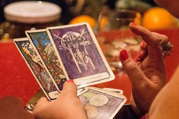 Hand with red nails holding a spread of tarot cards over a table