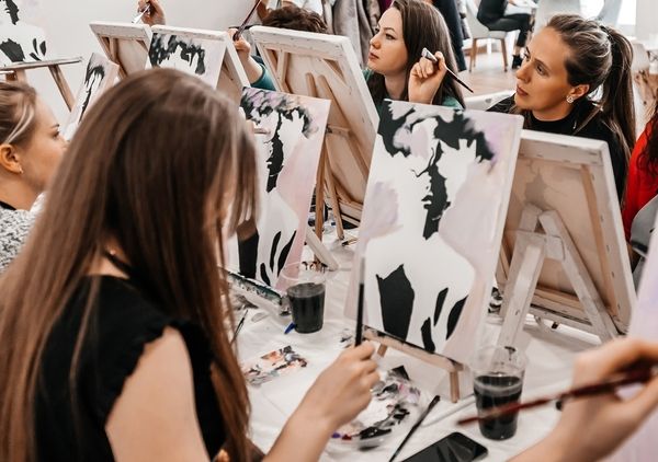 Friends painting canvases together at a paint and sip class