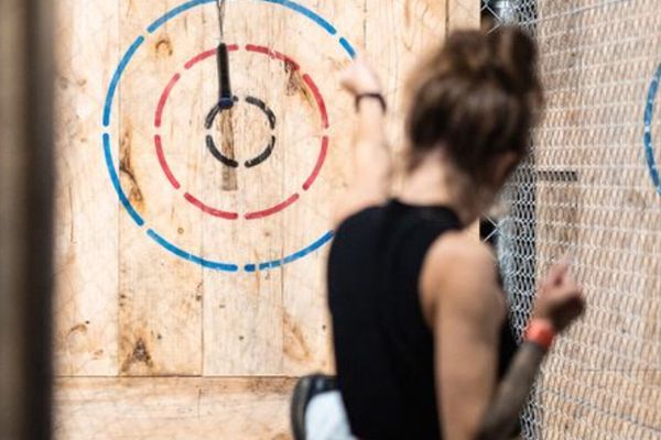 Woman in a black top throws an axe at a wooden bullseye target