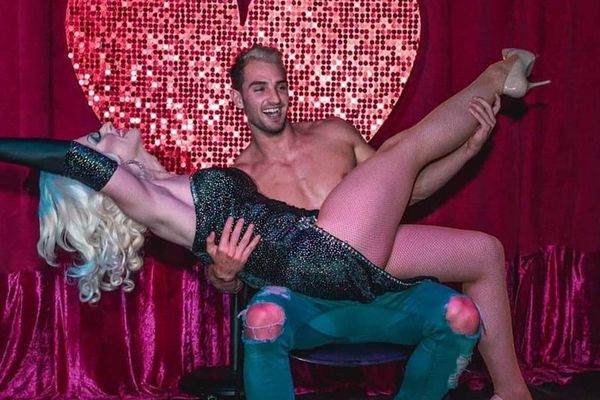 Shirtless performer dips a laughing blonde guest on stage in front of a sequin heart