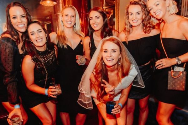 Hens group in black dresses around the bride in a veil in a copper-toned bar