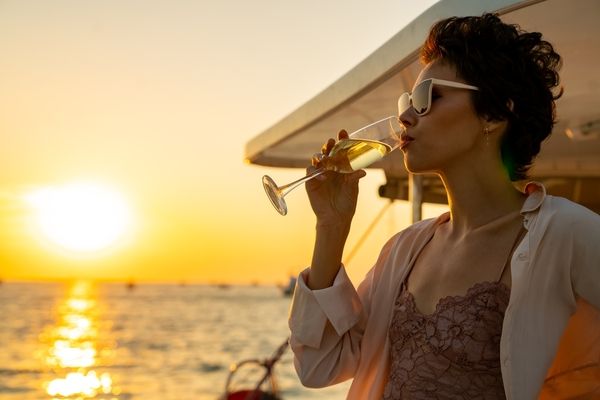 A woman sipping bubbles on a boat deck at sunset