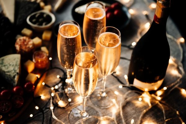 Glasses of bubbles and a bottle beside a cheese board and fairy lights