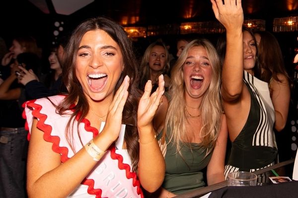 A bride to be in her sash cheering with friends in a crowded club