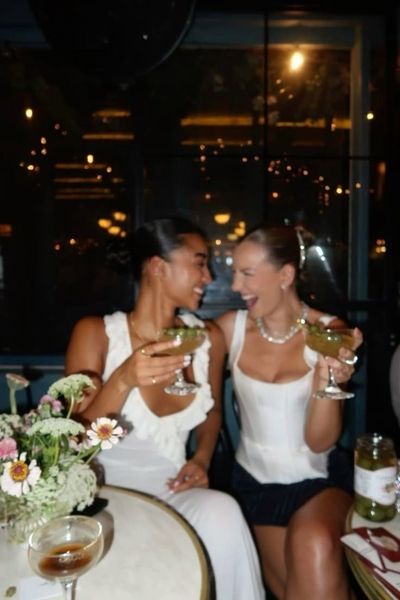 Two friends laughing over cocktails at a candlelit table