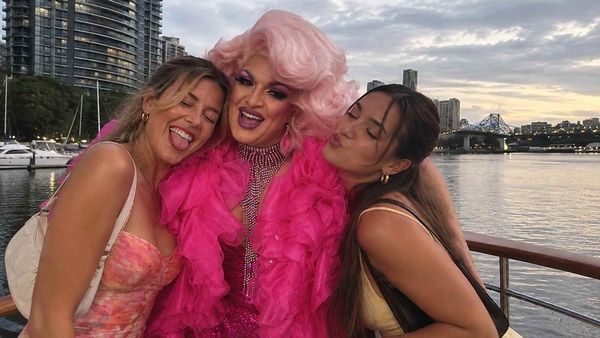 A drag queen in a pink feather boa with two friends by the river