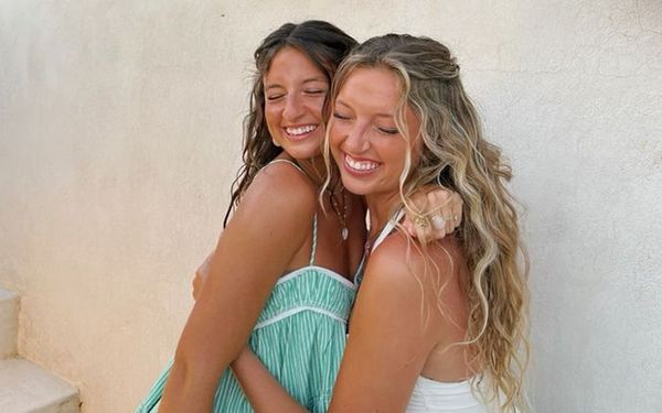 Two friends in summer dresses hugging and laughing by a whitewashed wall
