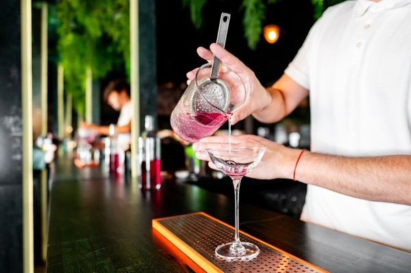 A bartender strains a pink cocktail into a coupe glass
