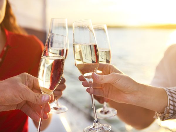 Friends clinking glasses of bubbles on a boat at sunset
