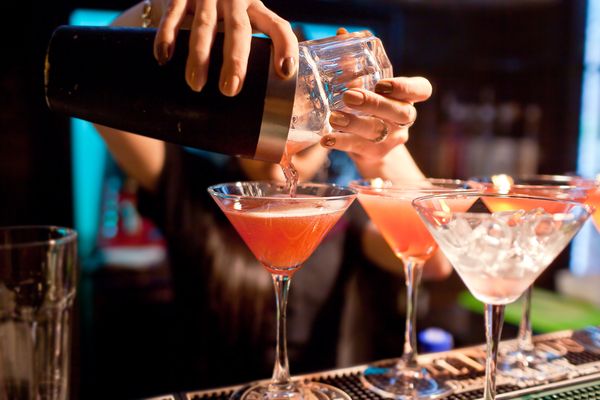 Hen pours her own mixed cocktail into a glass straight from the shaker over the bar counter during the cocktail making class