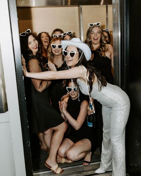 A hens group in heart sunglasses and a cowgirl hat squeezed into a doorway laughing