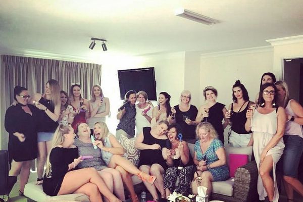 Large group of women laughing together on couches in a lounge room with drinks