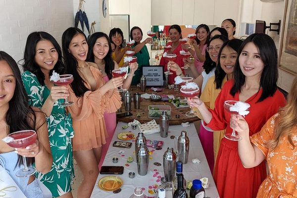 A hens group raising the cocktails they made along a long class table set with shakers