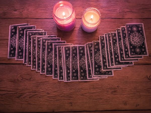 Tarot cards fanned across a wooden table between two candles