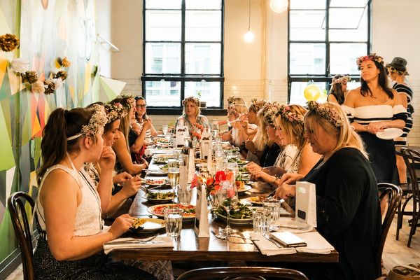 Women in flower crowns sharing a long dinner table in a bright restaurant