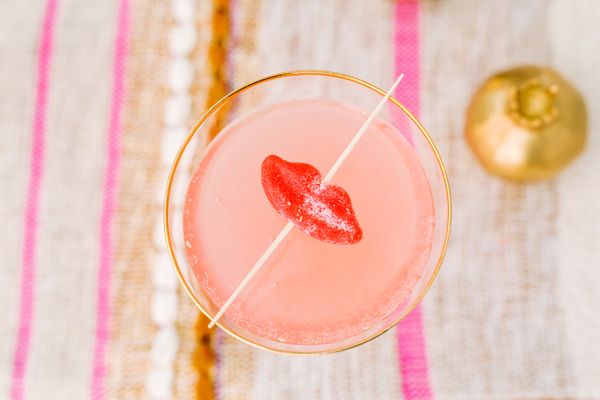 A delicious pink cocktail drink garnished with red lip candy