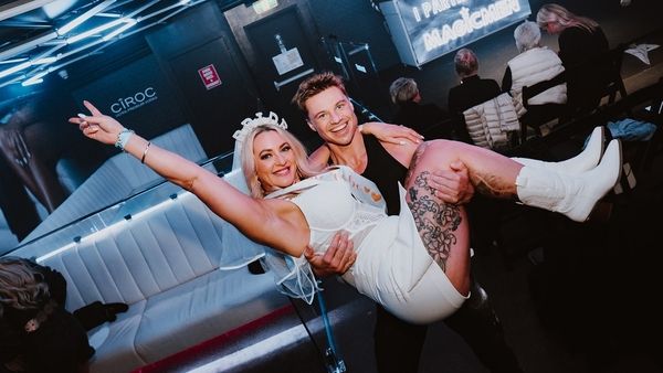 A man carrying a laughing bride to be in a tiara through a party bus
