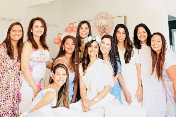 Smiling bride in a flower crown and sash with friends dressed in white and florals