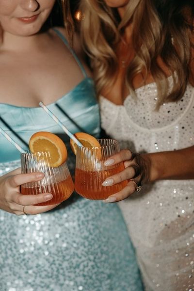 Two friends in sequins holding cocktails with orange slices