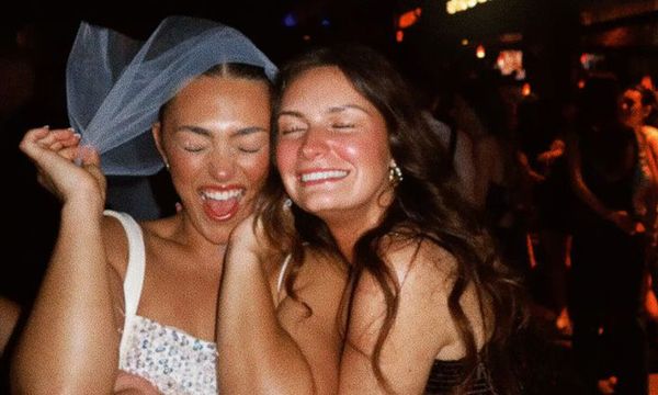 A bride to be in a short veil and her friend laughing cheek to cheek in a bar