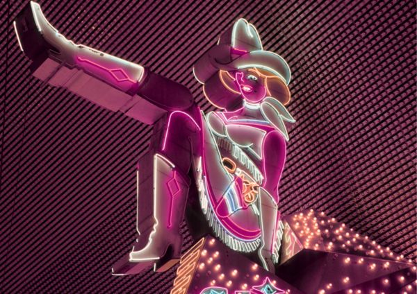 A pink neon cowgirl sign kicking one boot high
