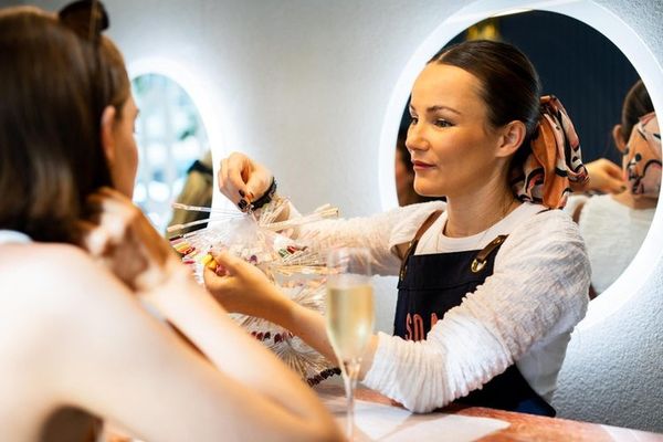 Nail artist holding colour swatches for a guest with a glass of bubbly nearby