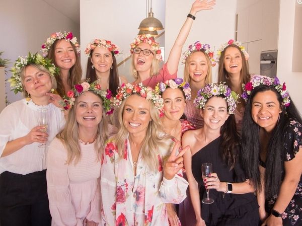 Friends in flower crowns cheering together in an apartment with glasses of bubbly