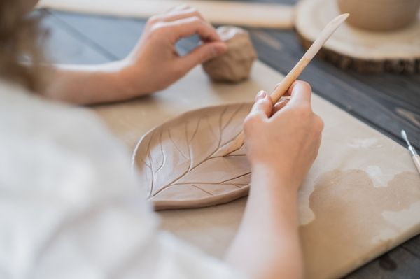 Hen is holding a brush and polishing a leaf shaped dish she created in her clay pottery session