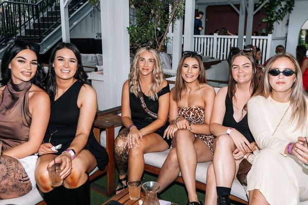 Seven women sitting together on outdoor lounges at a garden bar, smiling for the camera