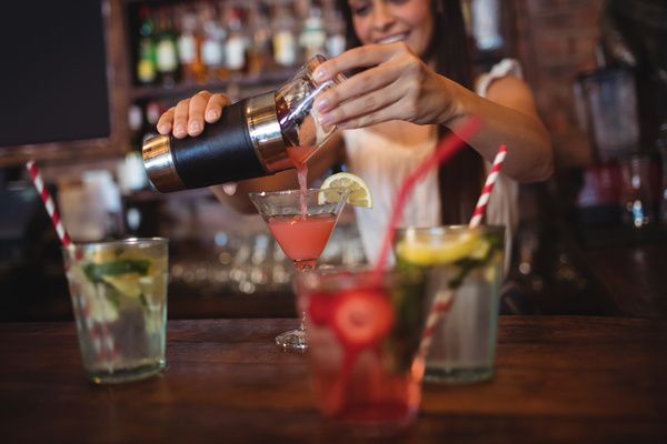 A gorgeous hen pours a blended cocktail from the shaker into glasses during the cocktail making class