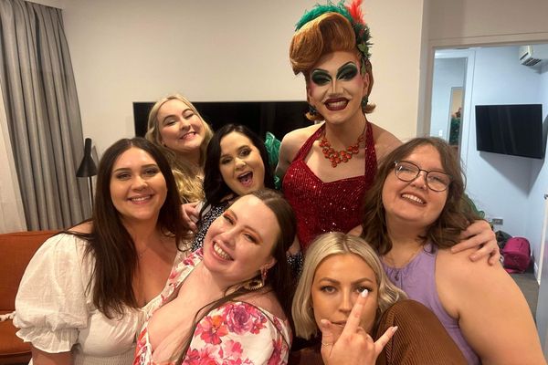 Drag queen in red sequins posing with a smiling group of women indoors