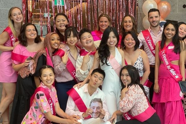 A big hens group in pink Team Bride sashes posing in front of pink tinsel