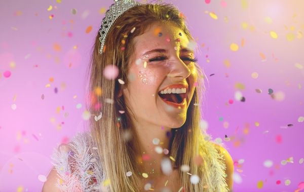 A lovely hen is laughing and wearing a tiara with a purple background and lots of falling confetti