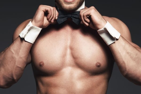A shirtless waiter straightening his black bow tie and cuffs