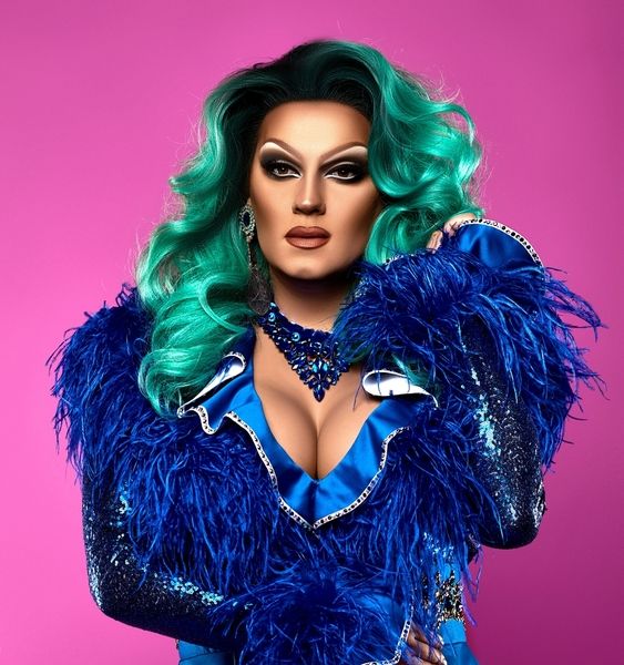 A stunning drag queen is wearing a feathery blue costume and blue green hair and preparing to perform for the hen party
