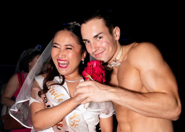 The bride in a veil and sash laughing with a topless waiter in a bow tie