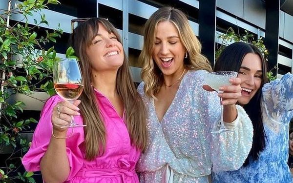 Friends in pink, white sequins and blue florals raising their glasses on a rooftop