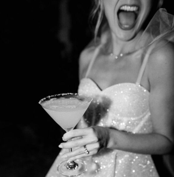A laughing bride to be in a veil holding a margarita, in black and white
